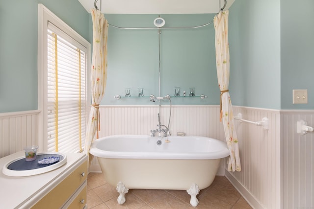 bathroom featuring a wainscoted wall, a freestanding bath, and tile patterned flooring