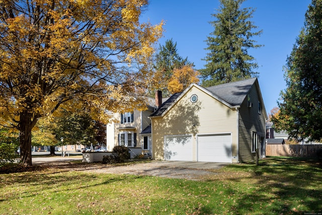 traditional-style house featuring a chimney, a front yard, fence, a garage, and driveway