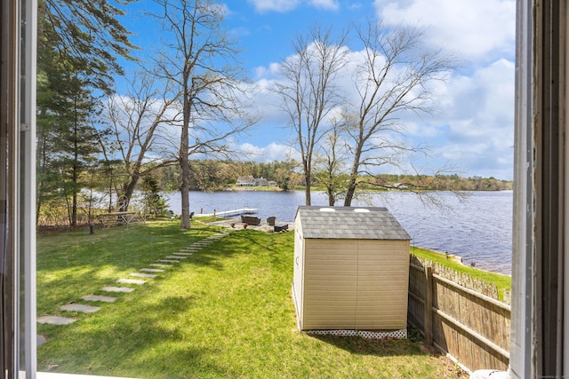 view of yard featuring a dock, a water view, fence, and a storage unit