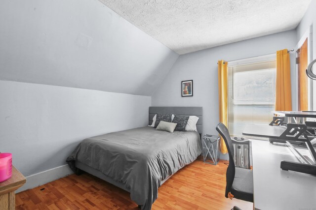 bedroom with lofted ceiling, light wood finished floors, baseboards, and a textured ceiling