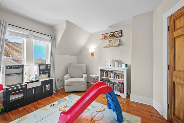 playroom featuring baseboards, wood finished floors, vaulted ceiling, baseboard heating, and a sink