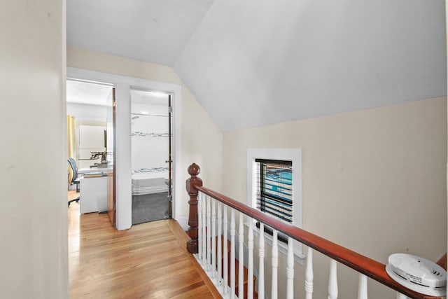 hallway with light wood-style floors, vaulted ceiling, and an upstairs landing