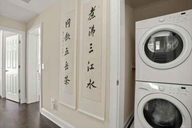 clothes washing area with stacked washer and dryer, dark wood-style flooring, and baseboards