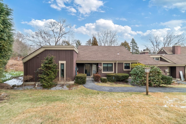 view of front of home with roof with shingles, a front lawn, a chimney, and driveway