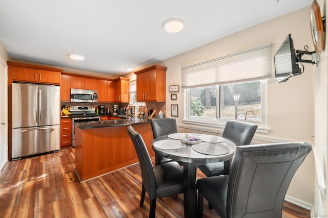 kitchen featuring dark wood-style floors, stainless steel appliances, dark countertops, a sink, and a peninsula