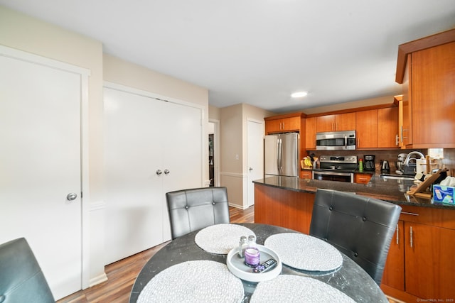 kitchen with light wood finished floors, brown cabinets, a peninsula, stainless steel appliances, and a sink