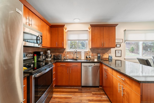 kitchen with decorative backsplash, appliances with stainless steel finishes, a sink, wood finished floors, and a peninsula