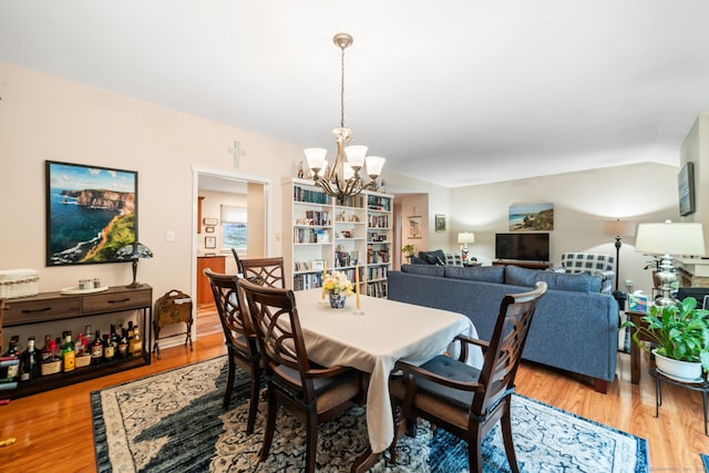 dining space featuring an inviting chandelier, vaulted ceiling, and wood finished floors