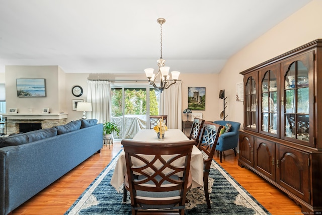 dining room featuring a chandelier, vaulted ceiling, a fireplace, and light wood finished floors