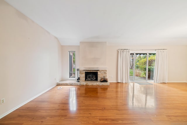 unfurnished living room featuring a stone fireplace, baseboards, and light wood-style floors