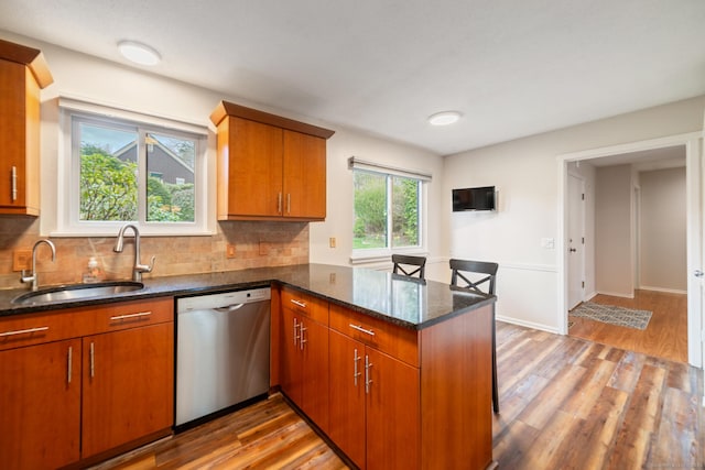kitchen with a peninsula, stainless steel dishwasher, a sink, and light wood finished floors