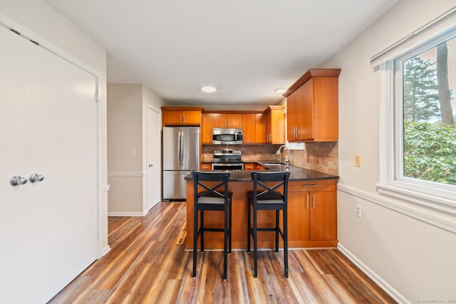 kitchen featuring a sink, brown cabinets, a healthy amount of sunlight, light wood-style flooring, and appliances with stainless steel finishes