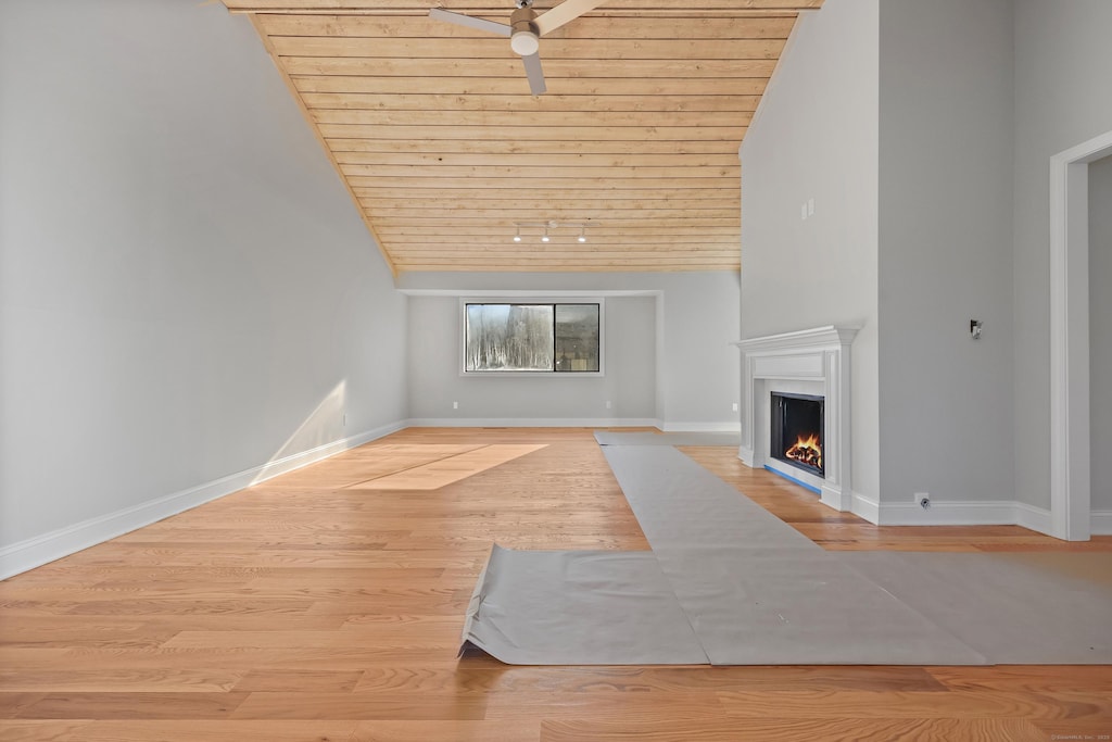 unfurnished living room featuring a ceiling fan, wood finished floors, a lit fireplace, baseboards, and wood ceiling