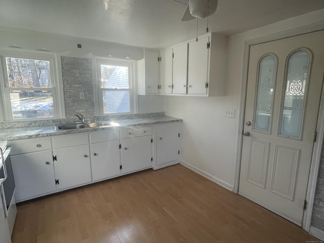 kitchen featuring light wood finished floors, white cabinets, a sink, and light countertops