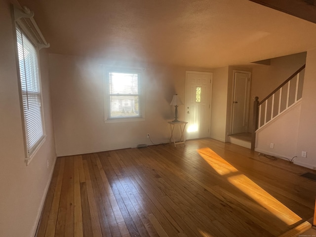 unfurnished living room featuring stairs, wood-type flooring, visible vents, and plenty of natural light