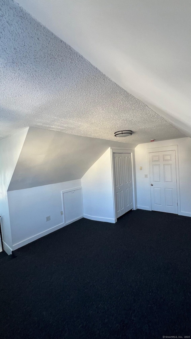 bonus room with lofted ceiling, baseboards, dark colored carpet, and a textured ceiling