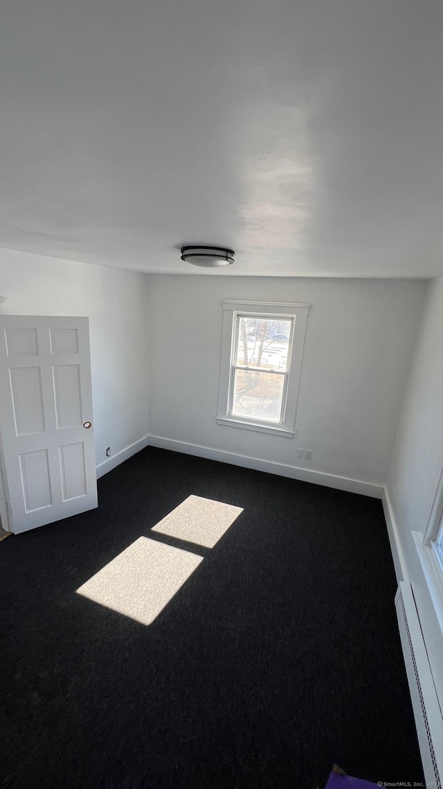 unfurnished room with a baseboard heating unit, dark carpet, and baseboards