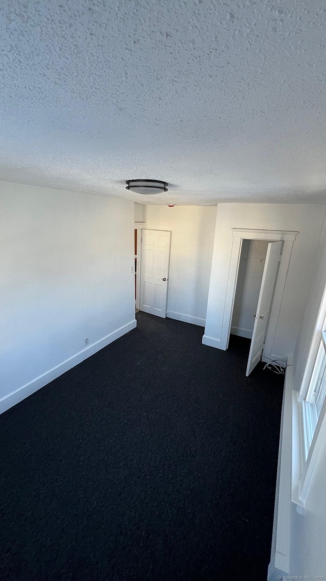 unfurnished bedroom with a textured ceiling, dark carpet, and baseboards