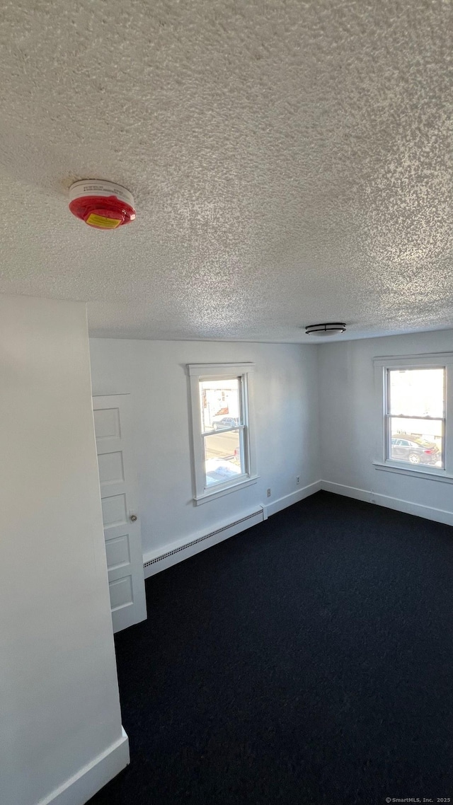 empty room with baseboards, dark carpet, baseboard heating, and a textured ceiling