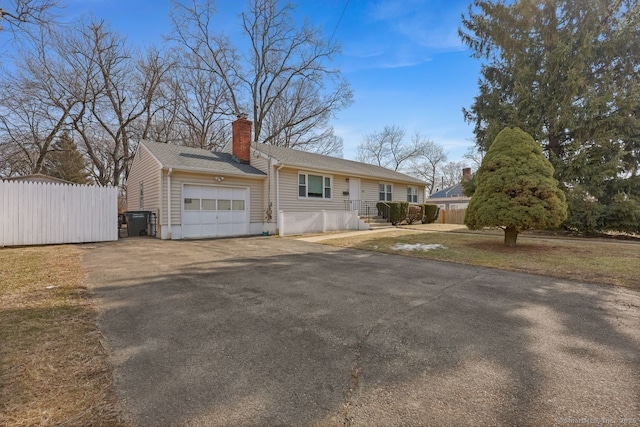 ranch-style house with driveway, a chimney, a garage, and fence