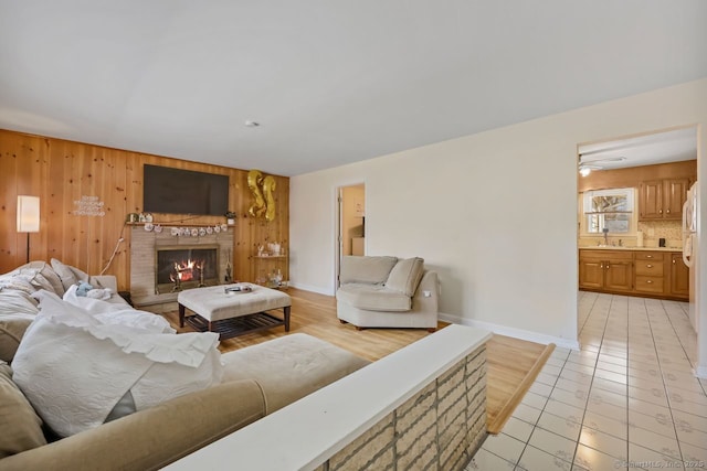 living area with light tile patterned floors, a lit fireplace, wooden walls, and baseboards