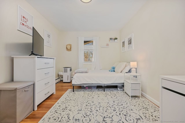 bedroom with light wood-style floors, a baseboard heating unit, and baseboards