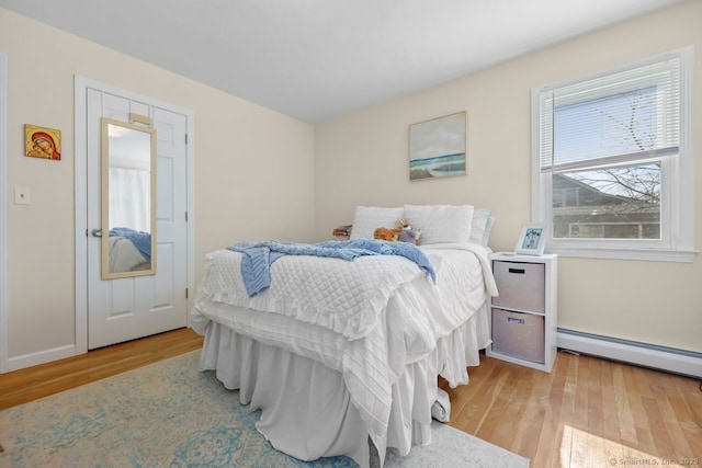 bedroom with baseboards, a baseboard heating unit, and wood finished floors