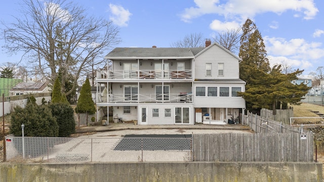 rear view of house with a balcony, a fenced front yard, a chimney, and a patio