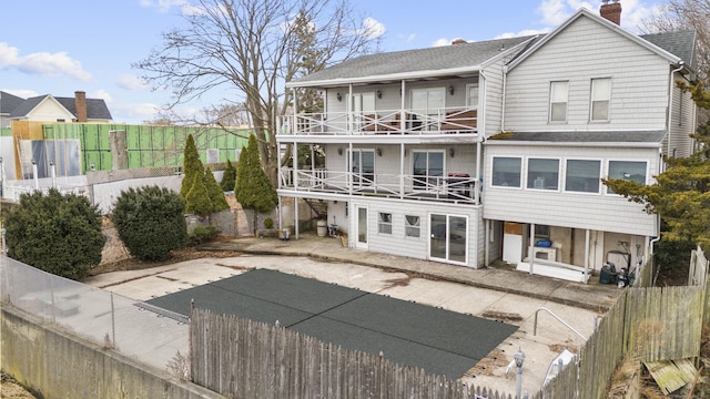 rear view of property featuring a shingled roof, a fenced backyard, a patio, and a balcony