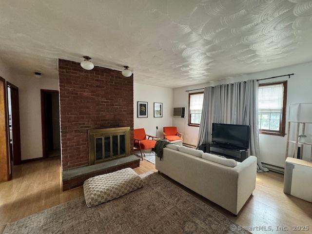 living room with a baseboard heating unit, a textured ceiling, a fireplace, and wood finished floors