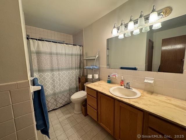 bathroom with toilet, a shower with shower curtain, vanity, tile walls, and tile patterned floors