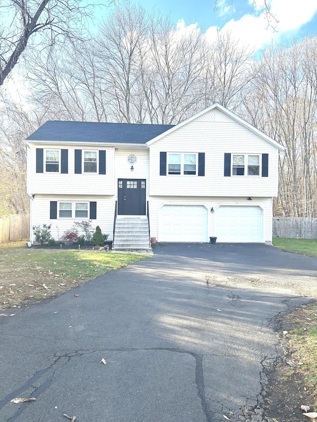 bi-level home featuring aphalt driveway, entry steps, fence, and a garage