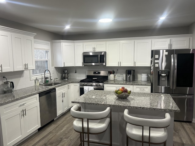 kitchen with stainless steel appliances, a sink, white cabinetry, backsplash, and dark wood finished floors