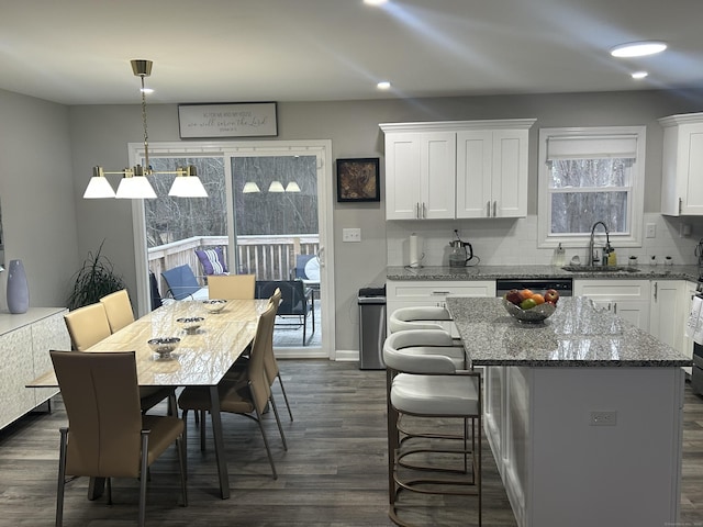 kitchen with dark wood finished floors, decorative backsplash, a kitchen island, white cabinetry, and a sink