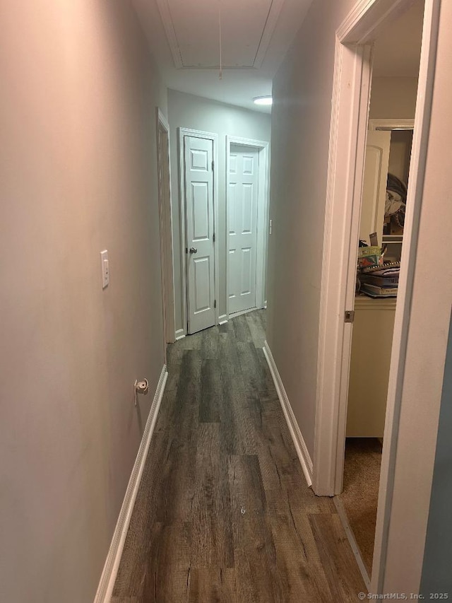 hall with attic access, dark wood-style flooring, and baseboards