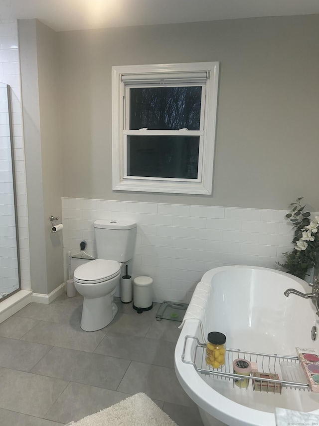 bathroom featuring a freestanding tub, toilet, a wainscoted wall, tile walls, and tile patterned floors