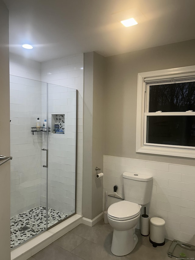 bathroom with tile patterned flooring, toilet, a wainscoted wall, tile walls, and a stall shower