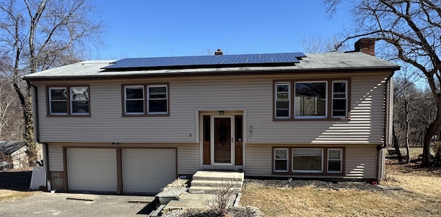 bi-level home with driveway, a chimney, solar panels, and a garage