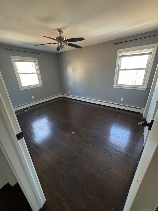 empty room featuring a ceiling fan, wood finished floors, a wealth of natural light, and a baseboard heating unit