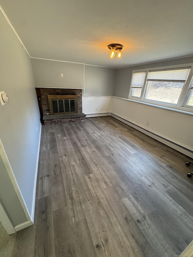 unfurnished living room with a brick fireplace, baseboard heating, wood finished floors, and baseboards