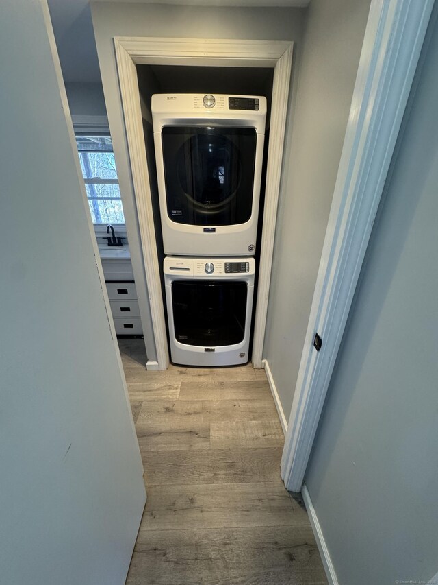 laundry area featuring stacked washer / drying machine, a sink, wood finished floors, laundry area, and baseboards