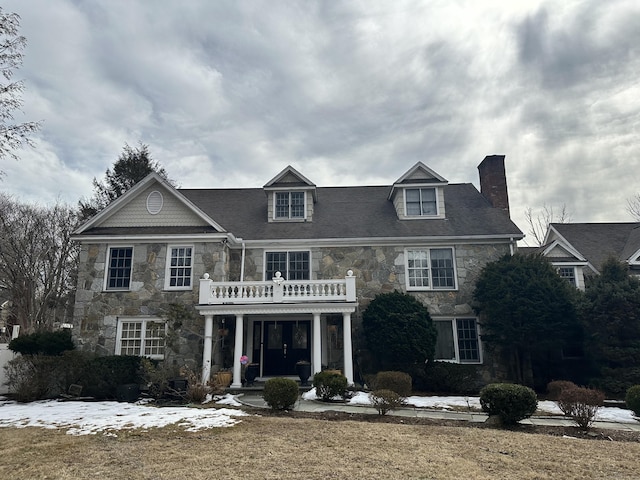 colonial home featuring a chimney, stone siding, and a balcony