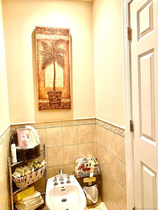 bathroom featuring a wainscoted wall, a sink, tile walls, and a bidet