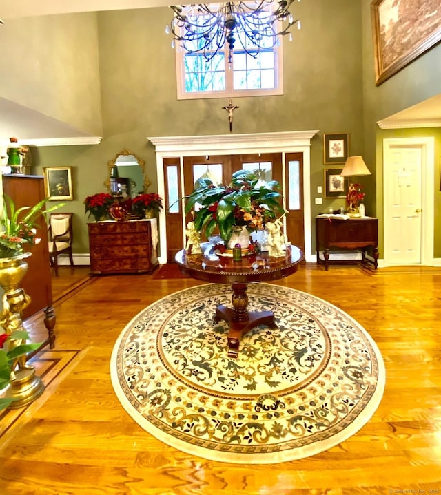 entrance foyer featuring a high ceiling, baseboard heating, wood finished floors, a chandelier, and baseboards