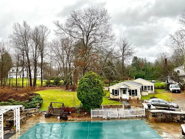 view of pool featuring a fenced front yard, a patio area, a lawn, and a covered pool