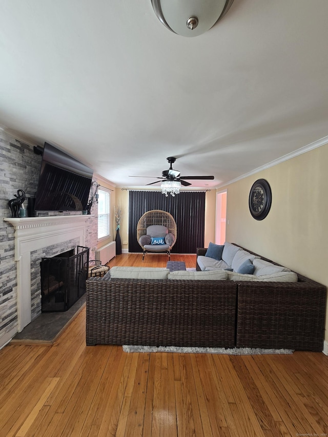 living area featuring a large fireplace, a ceiling fan, ornamental molding, and hardwood / wood-style floors