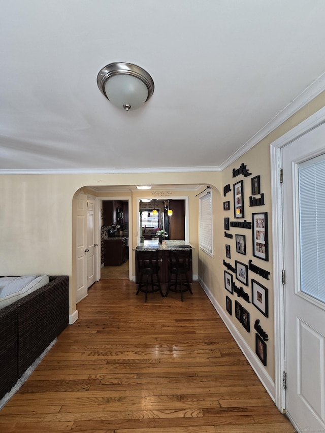 corridor featuring arched walkways, crown molding, baseboards, and wood finished floors