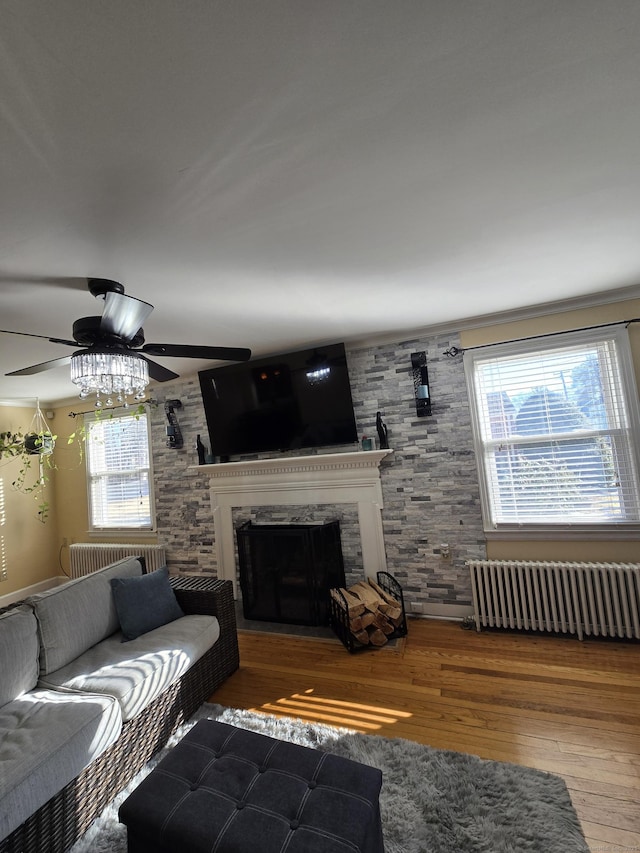 unfurnished living room with radiator, ceiling fan, a fireplace, and wood finished floors