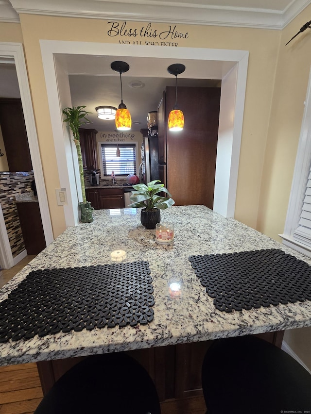 kitchen featuring light stone counters, refrigerator, crown molding, pendant lighting, and a sink