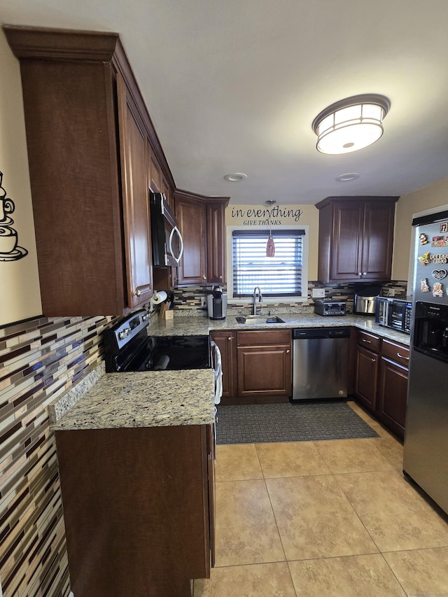 kitchen with light tile patterned floors, appliances with stainless steel finishes, a sink, dark brown cabinets, and light stone countertops